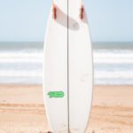 surfboard perfectly stuck in beach sand with ocean perpendicular in background in Essaouira Morocco by Susan Paige photography